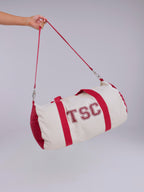 White and red duffel bag with 'TSC' branding held by a hand against a gray background